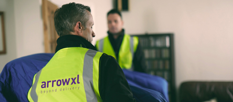 ArrowXL colleagues in hi-vis carrying a sofa into a customers home